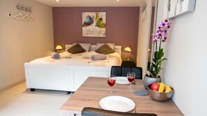 A hotel room with a bed, bedside tables, a dining table with chairs, a bowl of fruit, and a vase with flowers. - Studio (Soesterberg)