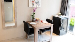 A dining area with a wooden table, black chairs, a small refrigerator, and a wall-mounted painting. - Studio (Soesterberg)