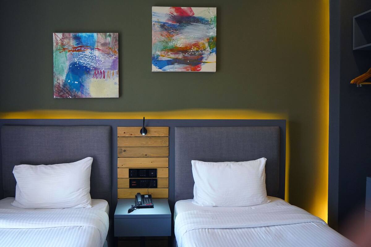 Habitación de hotel con dos camas, una mesita de noche con teléfono y dos cuadros abstractos en la pared.