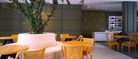 Un rincón interior acogedor con un sofá, sillones de mimbre, una mesita y un árbol decorativo.