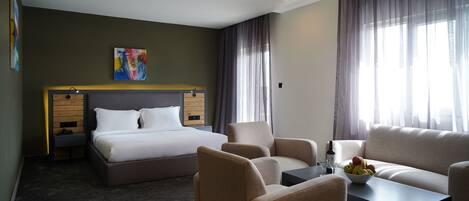 A hotel room with a bed, two armchairs, a sofa, a coffee table, and a painting on the wall.