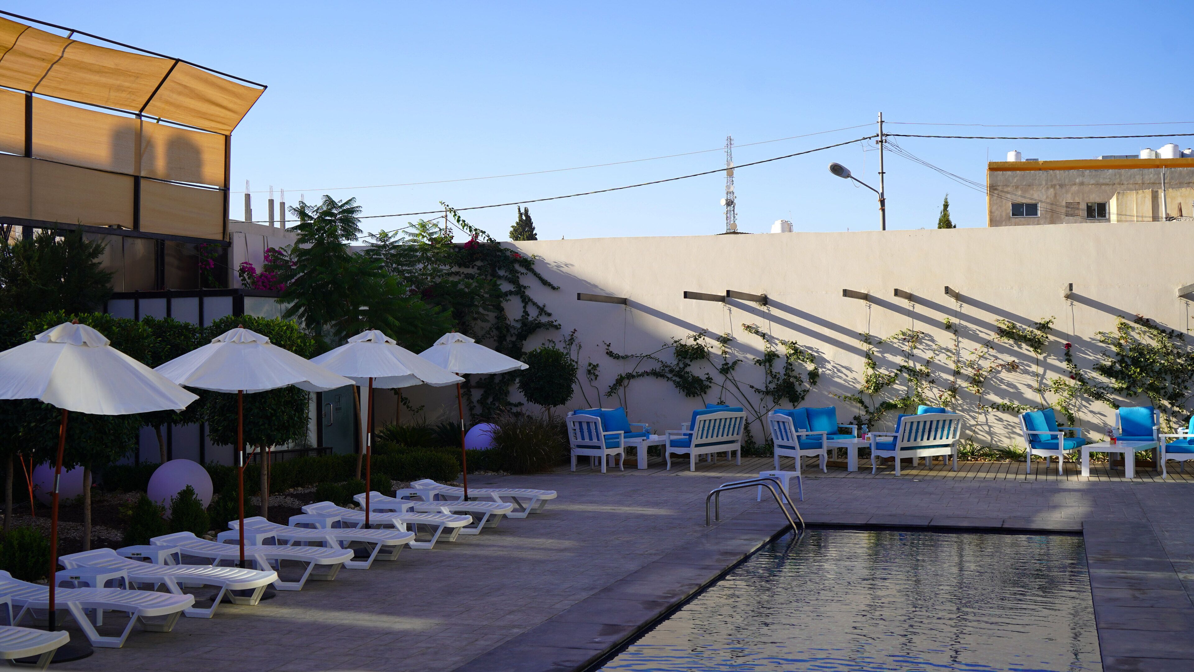 Uma área à beira da piscina com espreguiçadeiras, guarda-sóis e uma piscina.