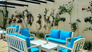 An outdoor patio with white furniture and blue cushions, a pergola, and climbing plants against a wall. - Aitch Boutique Hotel - an LIH Hotel (Madaba)