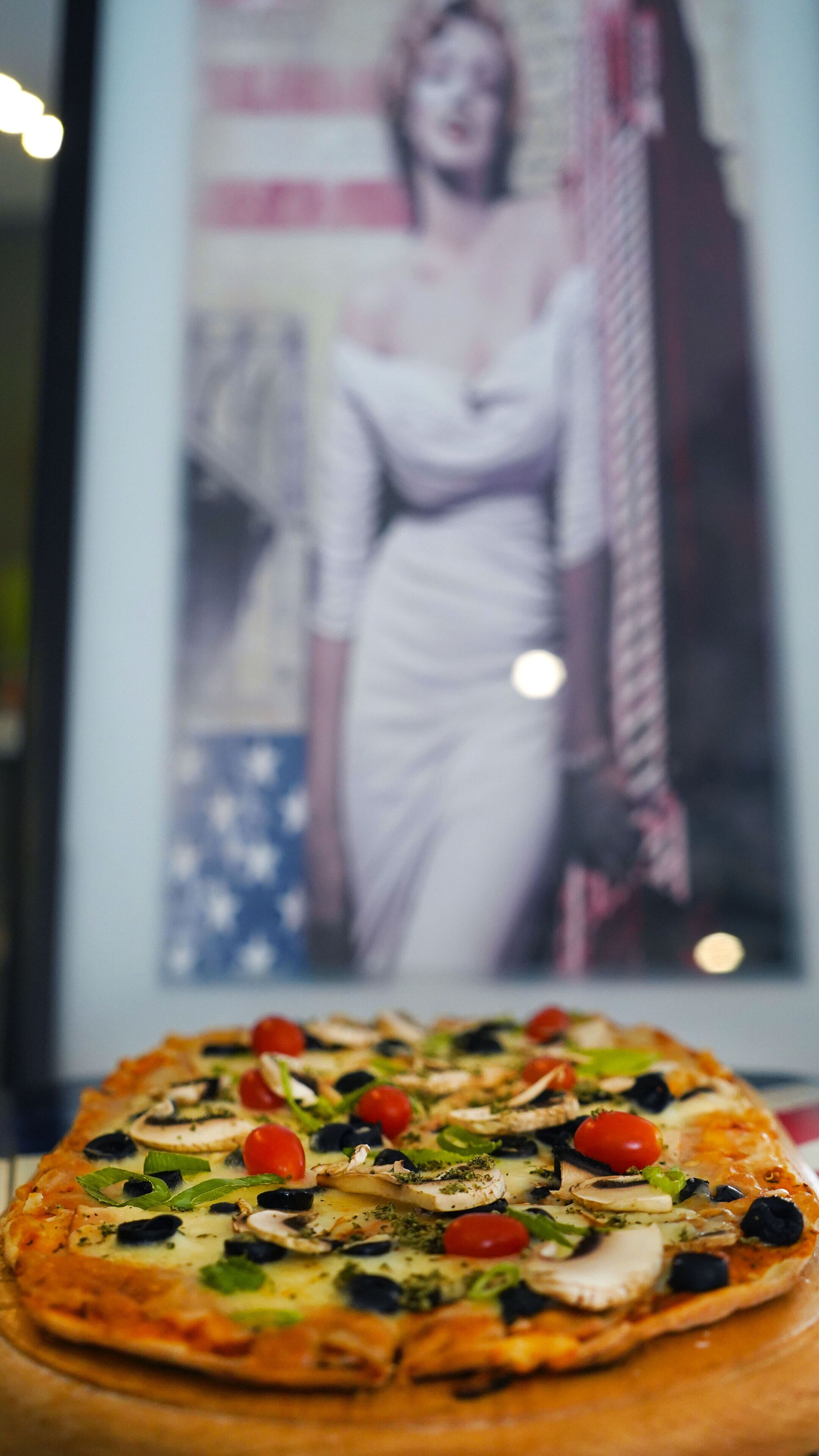 A pizza with various toppings in front of a framed picture.