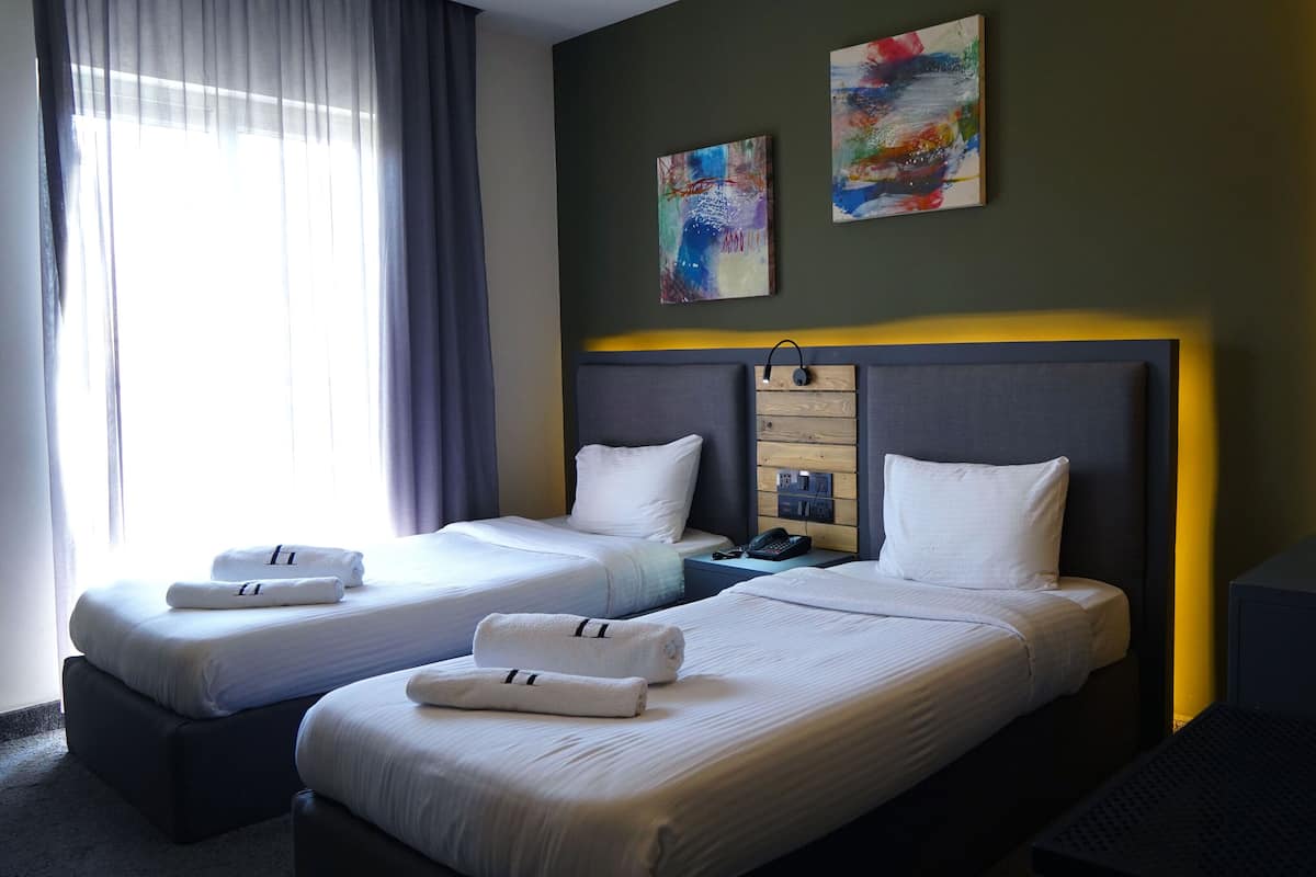 Habitación de hotel con dos camas, una mesita de noche con teléfono y una obra de arte en la pared.