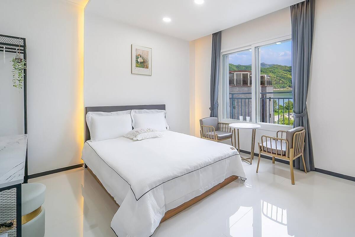 Une chambre d’hôtel moderne avec un grand lit, une petite table à manger et un balcon offrant une vue panoramique.