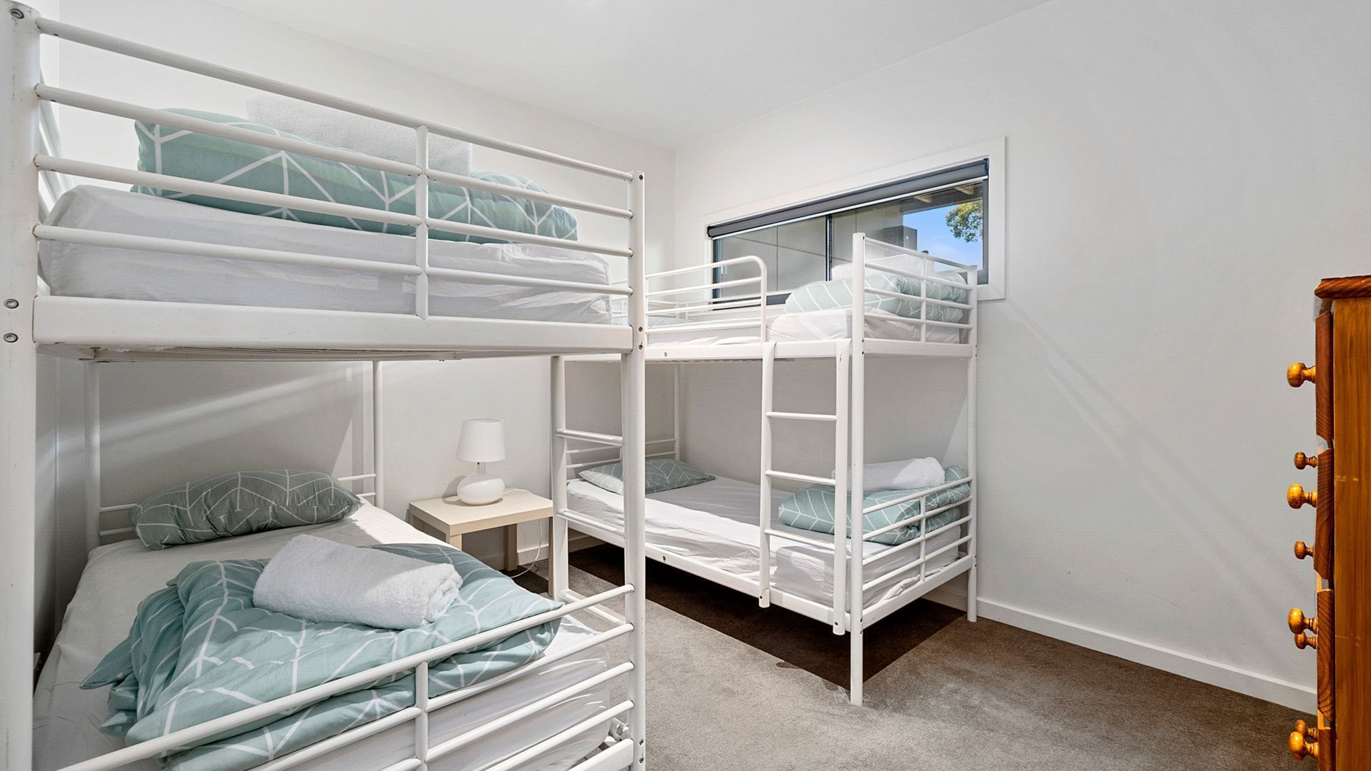 A dormitory room with bunk beds, a small bedside table with a lamp, and a window.