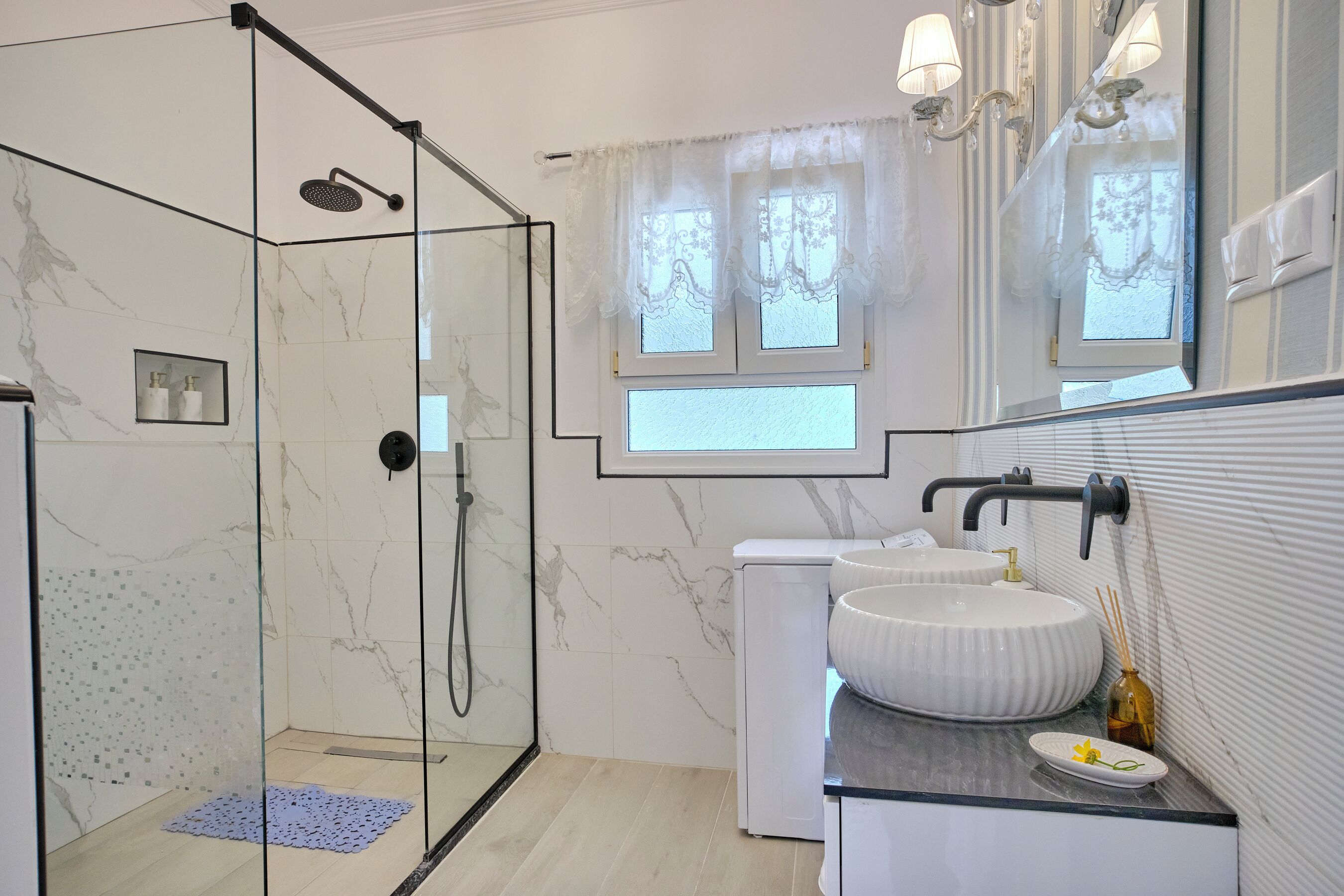 Ein modernes Badezimmer mit einer Duschkabine, einem weißen Waschbecken und einem Fenster mit dekorativen Vorhängen.