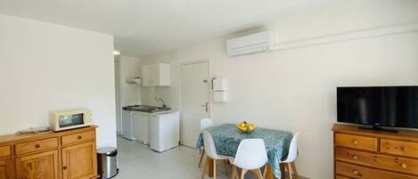Un espace de vie compact comprenant un coin cuisine, un coin repas avec une table et des chaises, un canapé, un téléviseur et un meuble en bois.