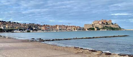 A coastal town with a prominent castle on a hill, a sandy beach, and a marina with boats.
