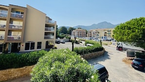 A multi-story residential building with balconies, a parking area, and a mountain backdrop. - Cozy 1-Bedroom Apartment with Terrace, 100m from Beach, Parking Included - Calvi (Calvi)