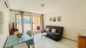 A living room with a sofa, a dining table with chairs, a window with curtains, and a small table with a fruit bowl. - Cozy 1-Bedroom Apartment with Terrace, 100m from Beach, Parking Included - Calvi (Calvi)