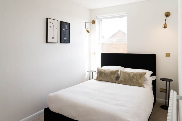 A bedroom with a bed, two bedside tables, a window, and wall-mounted artwork.