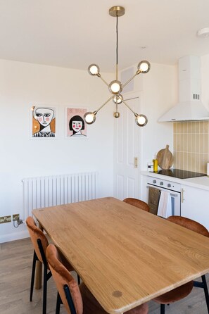 A modern kitchen with a central island, white cabinetry, a stainless steel range hood, and a pendant light fixture.