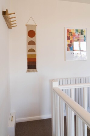 A staircase with a white railing, a wall-mounted tapestry with geometric patterns, and a framed abstract painting.