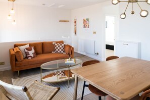 A modern living room with a sofa, a glass coffee table, a wooden dining table, and a patterned rug.
