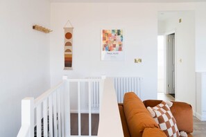 A room with a white crib, a brown sofa with a checkered throw, and a wall with a colorful abstract painting and a wooden wall art piece.