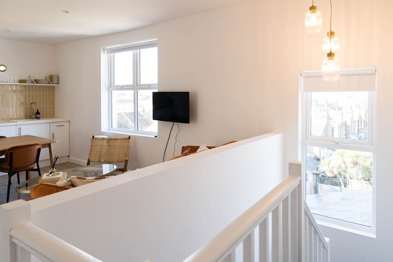 Een moderne woonkamer met een glazen salontafel, een flatscreen televisie aan de wand en een eethoek met een houten tafel en stoelen.