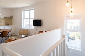 A modern living room with a glass coffee table, a flat-screen TV mounted on the wall, and a dining area with a wooden table and chairs.
