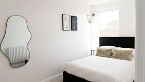 Un dormitorio con cama, radiador, espejo sujeto a la pared y dos cuadros enmarcados.