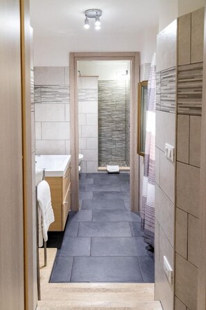 Ein schmales Badezimmer mit einem weißen Waschbecken, einer Toilette und einer Duschkabine.
