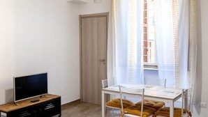 Um quarto pequeno e bem iluminado com uma mesa de jantar e cadeiras, uma televisão e um aparelho de ar condicionado.