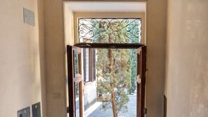 Uma escadaria de mármore leva a uma porta aberta com um portão de metal, um vaso de planta e uma pequena área externa com uma árvore.