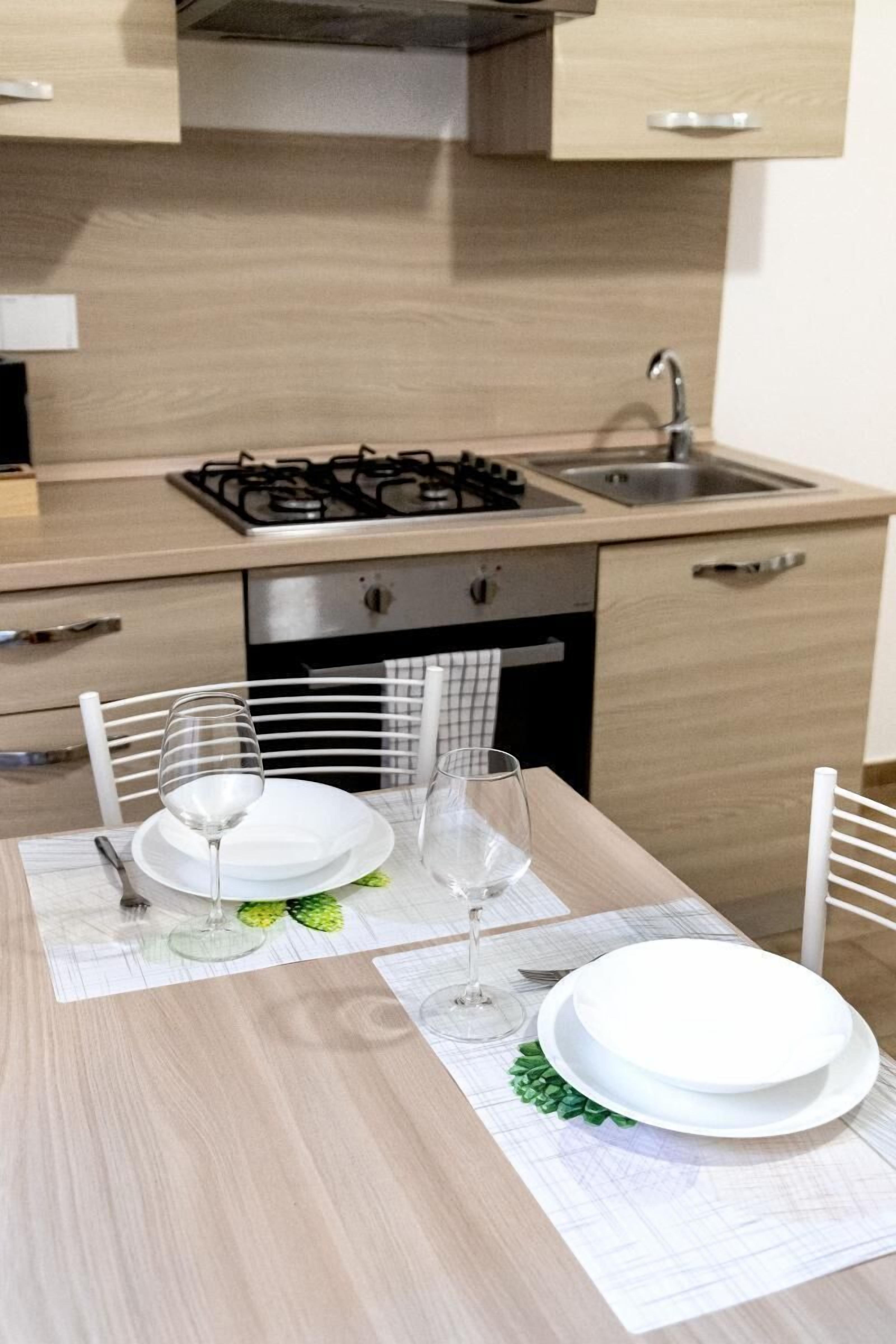 Une cuisine moderne équipée d’une cuisinière à gaz, d’un évier et de meubles en bois. On y trouve une table à manger mise avec des assiettes, des verres et une garniture verte.
