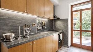A modern kitchen with wooden cabinets, a stainless steel sink, and a window with a view of greenery. - AR ROOMS ROME   blue room superior (ROMA)
