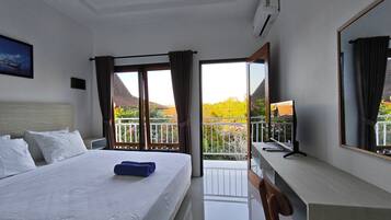 Habitación de hotel con cama, escritorio, silla, un espejo grande y balcón con vistas a zonas verdes y edificios.