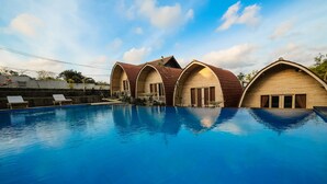A swimming pool with four wooden cottages, each with a pitched roof and a small balcony. - Puri Sadewa Balangan (Jimbaran)