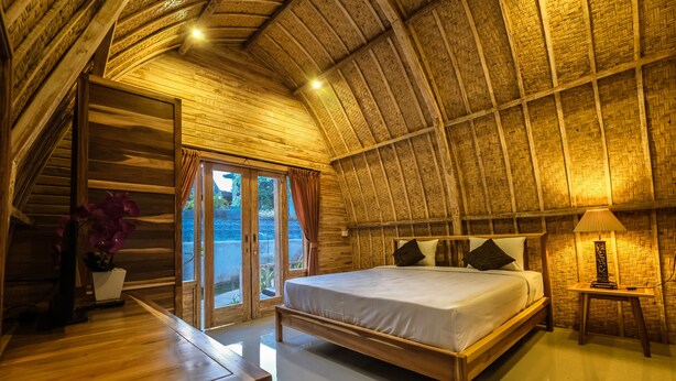 A room with a wooden ceiling, a bed with pillows, a bedside table, and a lamp. - Puri Sadewa Balangan (Jimbaran)