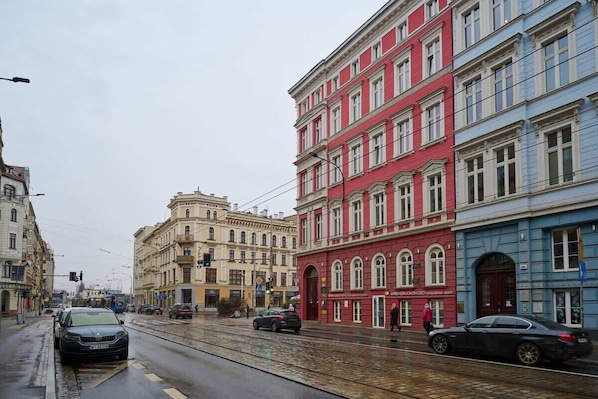 A street with tram tracks, multi-story buildings, and parked cars.