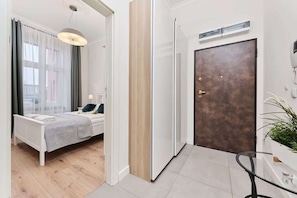 A modern hotel room with a bed, bedside table, and a view through a window with sheer curtains.