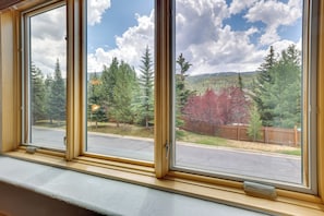 A window with a view of a road, trees, and a mountain range.