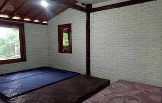 Una habitación con paredes de ladrillo blanco, techo de madera y una ventana. Hay dos camas con colchas estampadas.