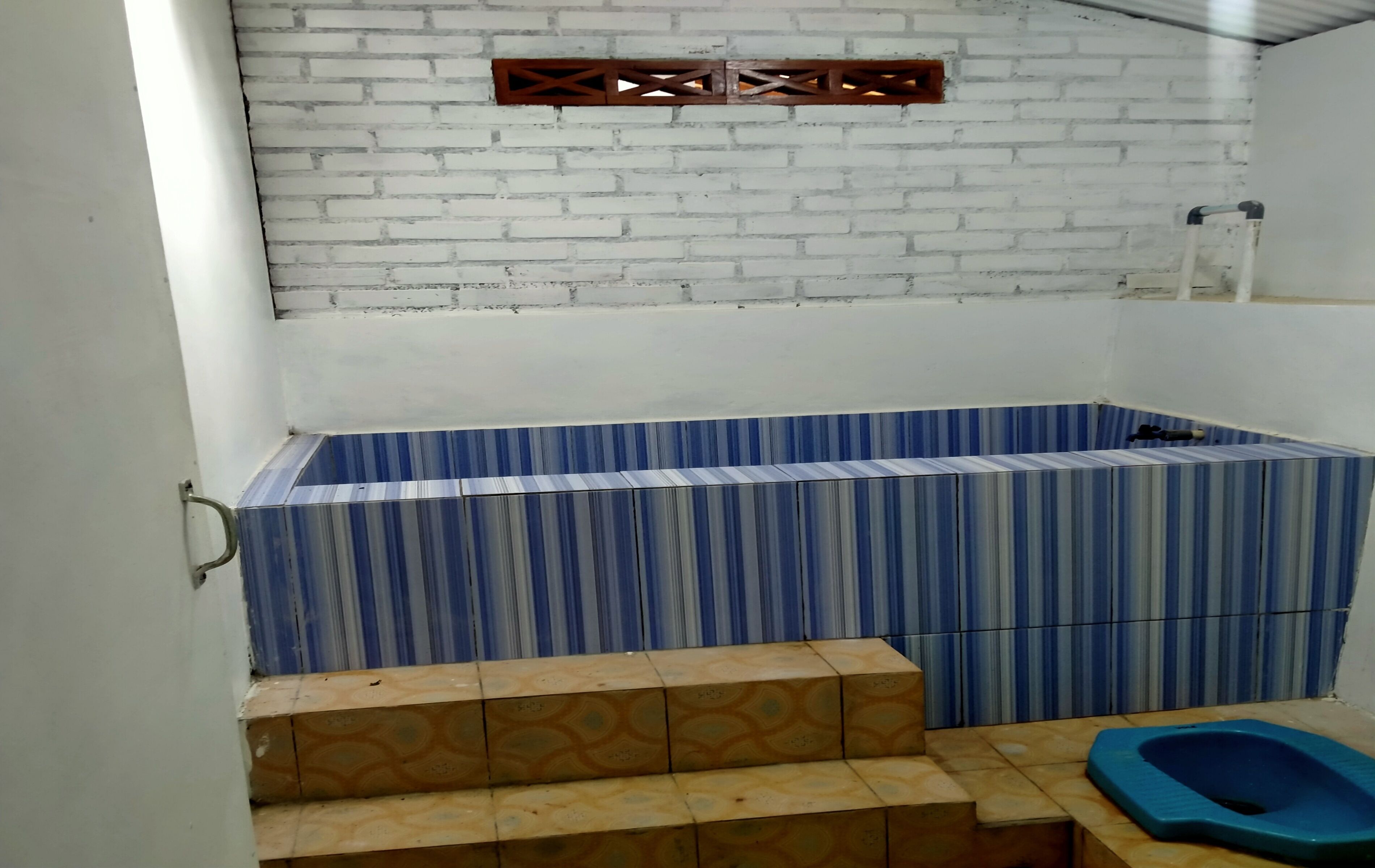 Een badkamer met een witte baksteenmuur, een badkuip met blauwe strepen en een blauw toilet.