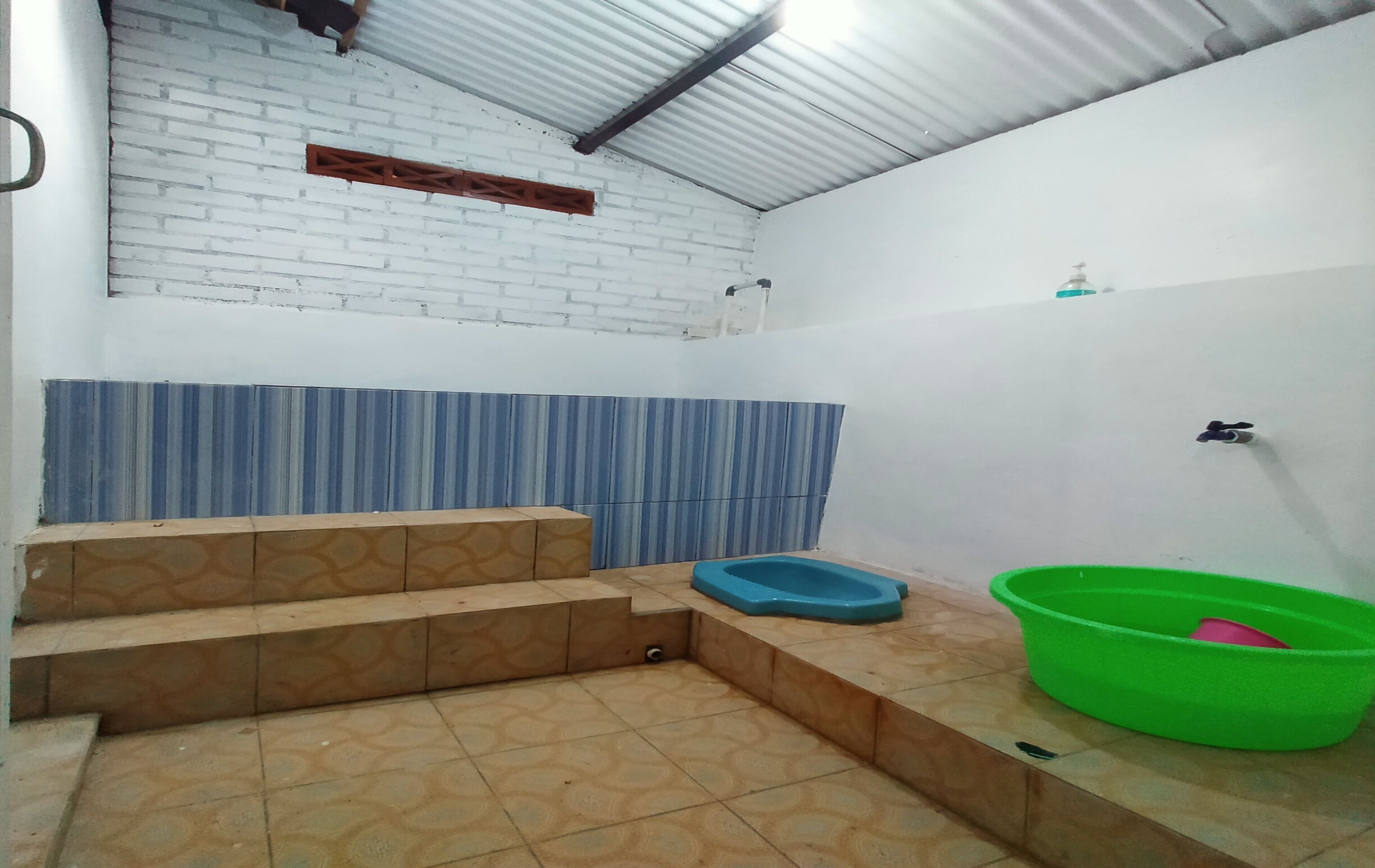 A bathroom with a tiled floor, a blue basin, a green basin, and a white wall with a blue-striped section.