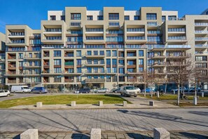 Un edificio residencial de varios pisos con balcones, un patio empedrado y coches aparcados.