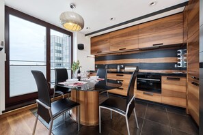 A modern kitchen with wooden cabinets, a black and white backsplash, and a dining area with a glass table and chairs.