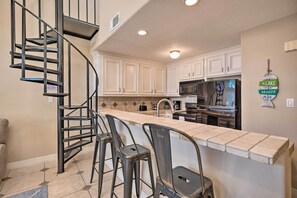 A kitchen with a central island, a spiral staircase, and white cabinets. - Idyllic Montgomery Condo w/ Pool & Lake View! (Montgomery)