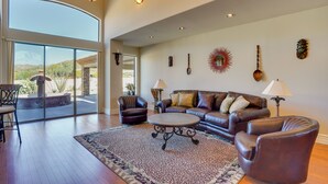 A spacious living room with a large window, leather furniture, and decorative wall art. - Outdoor Oasis! Group-Friendly Cave Creek Retreat (Cave Creek)