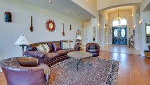A spacious living room with a brown leather sofa, a round coffee table, and a patterned rug. There are decorative wall hangings and a chandelier. - Outdoor Oasis! Group-Friendly Cave Creek Retreat (Cave Creek)