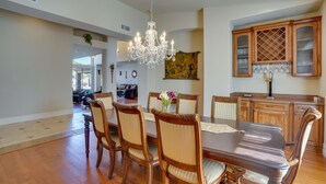 A dining room with a large wooden table, six chairs, and a chandelier. There is a kitchen area with wooden cabinets and a wine rack. - Outdoor Oasis! Group-Friendly Cave Creek Retreat (Cave Creek)