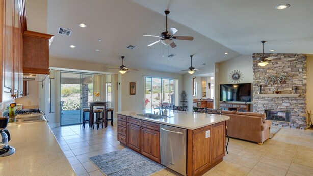 A spacious kitchen with a large island, wooden cabinets, and a built-in dishwasher. There are ceiling fans, a stone fireplace, and a large TV. - Outdoor Oasis! Group-Friendly Cave Creek Retreat (Cave Creek)