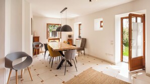 A modern dining area with a wooden table and chairs, pendant lighting, and a view of the outdoors through a glass door.