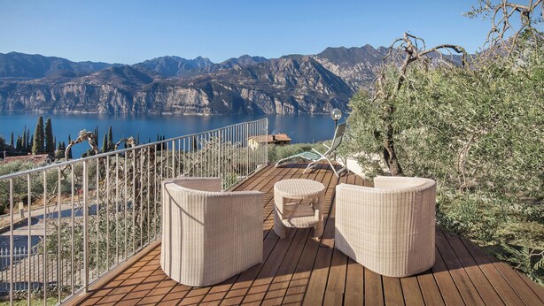A deck with wicker furniture overlooking a lake and mountains.