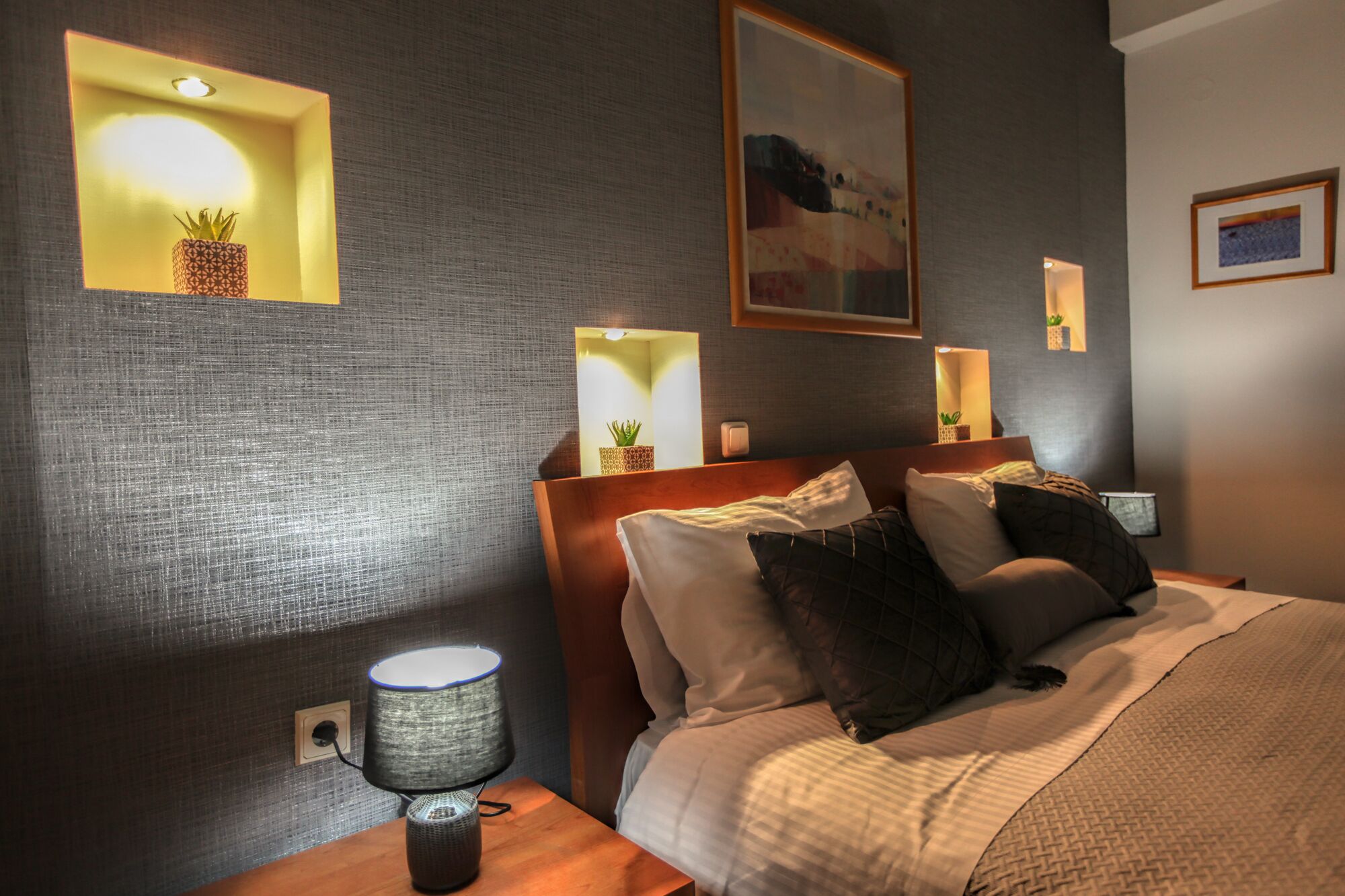 A hotel room with a bed, nightstands, wall-mounted lamps, and a painting.