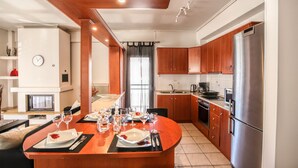 A modern kitchen with wooden cabinets, a stainless steel refrigerator, and a dining area with a round table set for four. - Grand Meteora Central Luxury Apartment (Kalabaka)