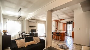 A modern living room with a black sofa, a coffee table with a decorative object, and a dining area with a wooden table and chairs. - Grand Meteora Central Luxury Apartment (Kalabaka)